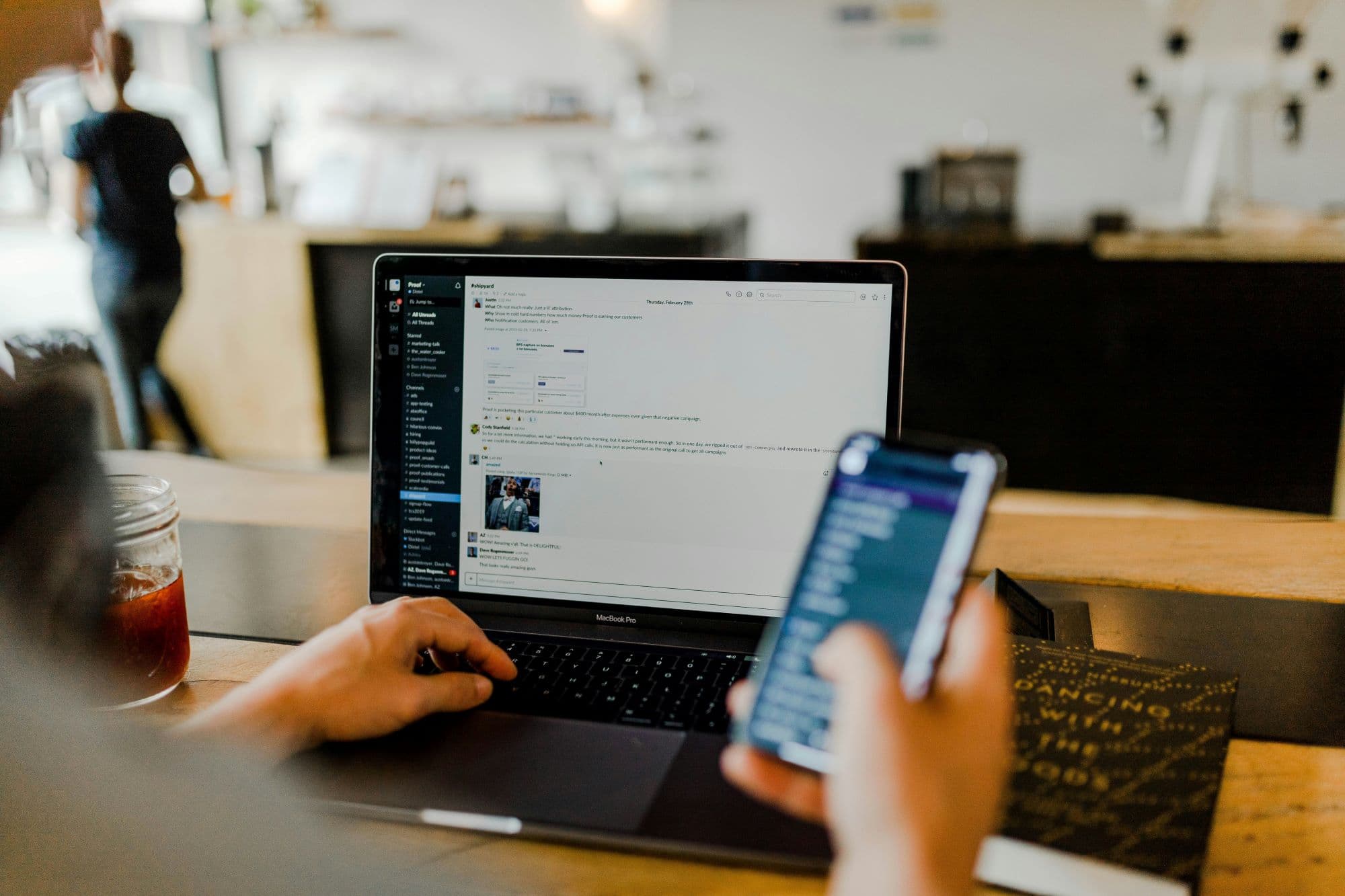 Person using mobile phone with blurred laptop in background